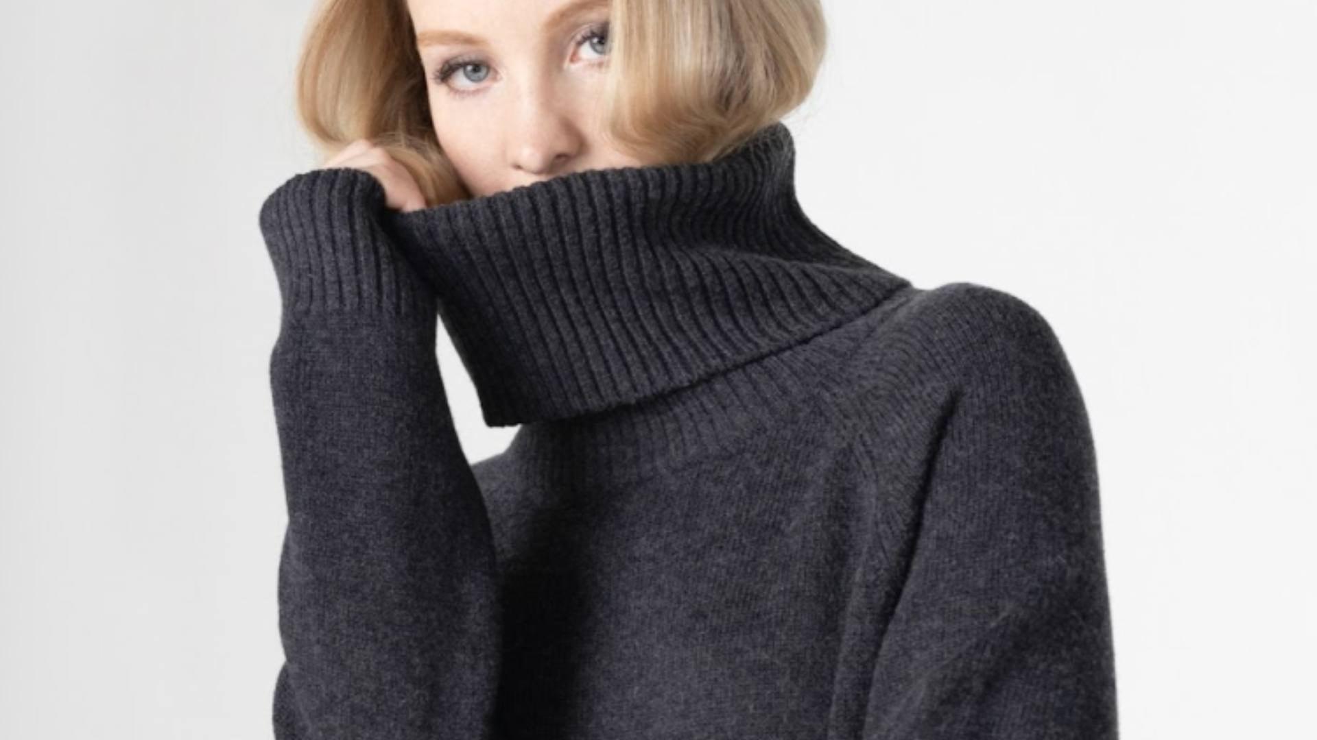 A blonde woman wears a dark gray turtleneck and poses for the camera, demonstrating cozy loungewear.