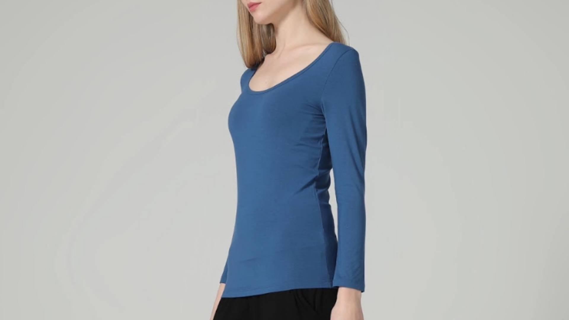 A woman wears a blue long sleeve t shirt and poses with her body facing the left direction.