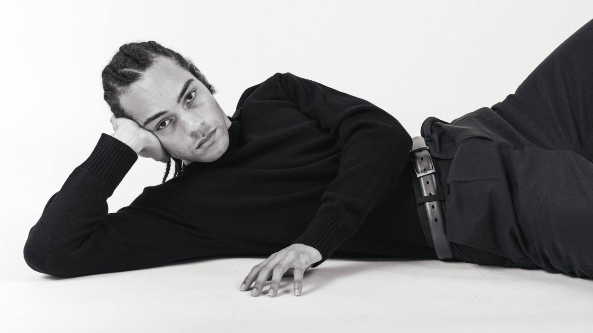 A man lays on the floor and faces the camera while wearing stylish, sustainable clothing from Not Labeled. The photo is in black and white.