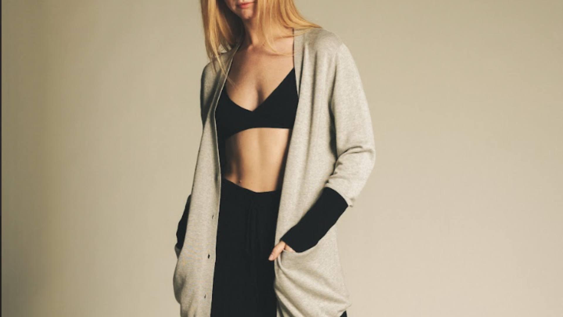 A blonde woman wears a cozy gray sweater with black sweatpants and a black bra, demonstrating luxe loungewear.