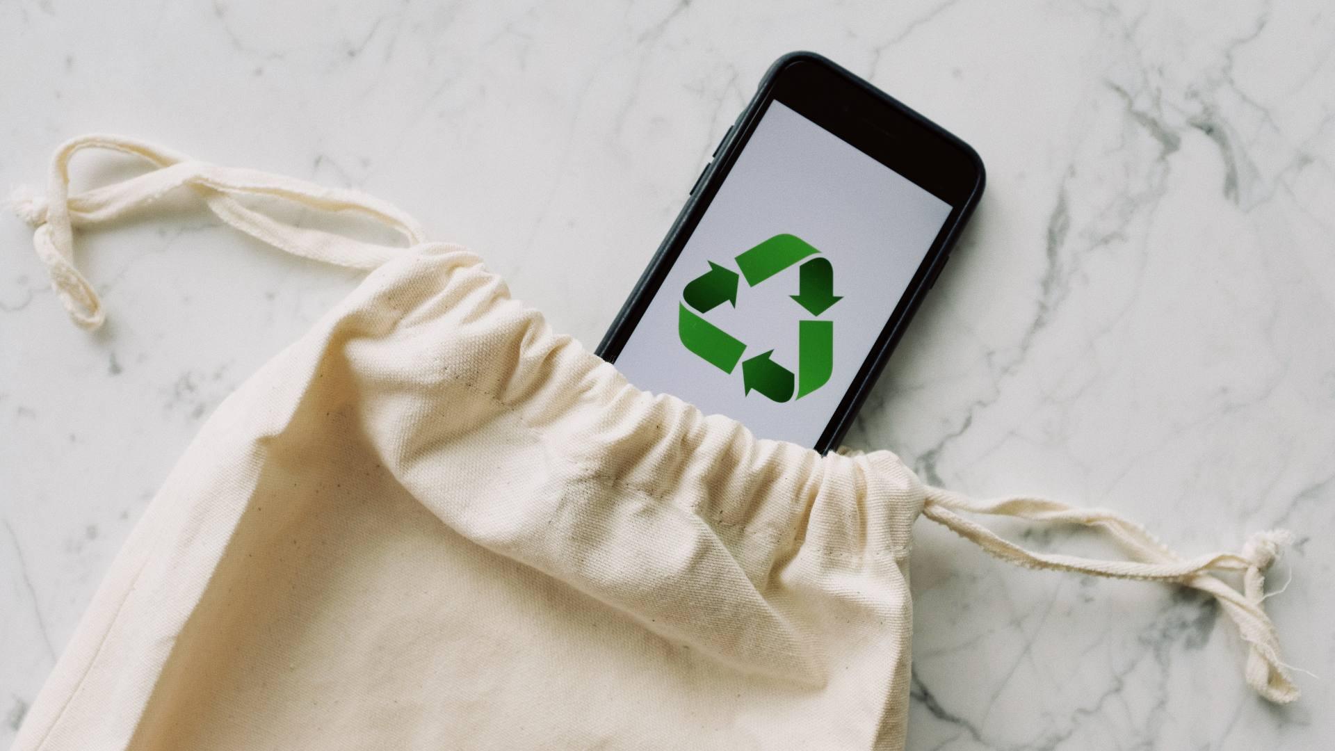 A white cloth bag is displayed with a phone coming out and a recycle symbol on it.