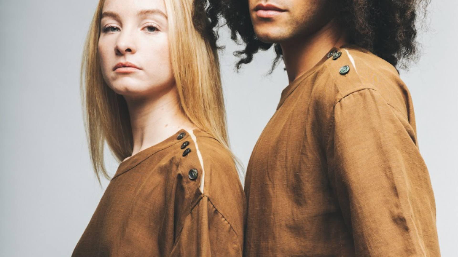 Two people stand together wearing sustainable brown tops.