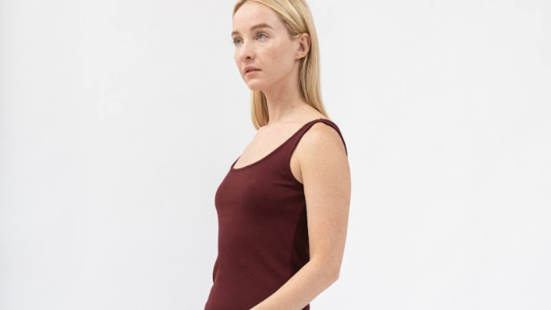 A blonde woman stands wearing a burgundy tank top, demonstrating sustainable clothing styles.